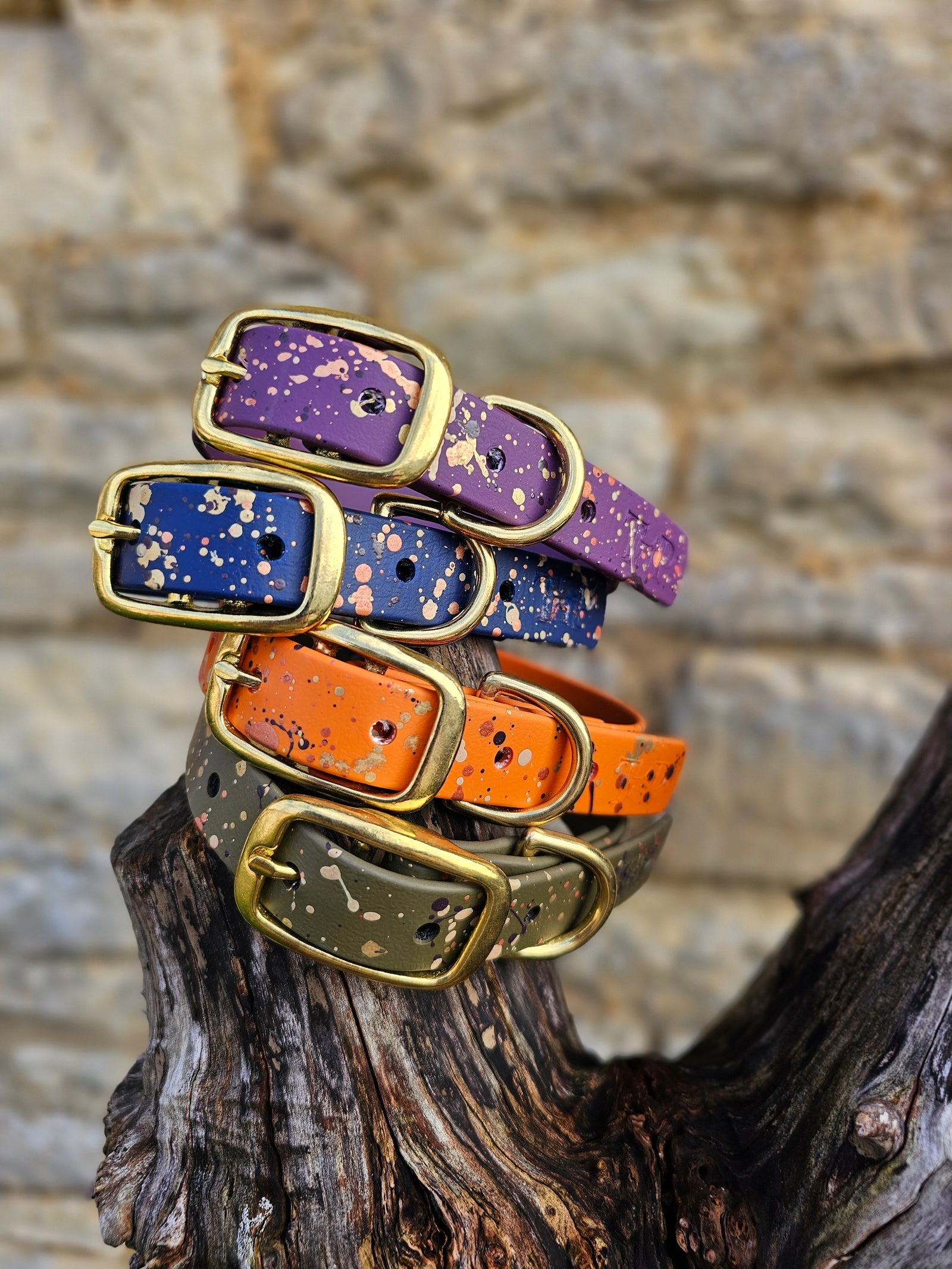 Trinkety Paws splatter collars in purple, navy, orange and olive, stacked on driftwood
